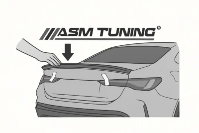 Hand pressing a spoiler onto the trunk of a BMW to test fitment before permanent installation, demonstrating alignment and positioning