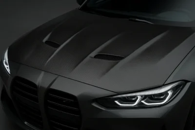 Close-up view of a BMW M4 with a dry carbon fiber featuring dual heat extractors, showcasing a lightweight performance design and premium weave texture