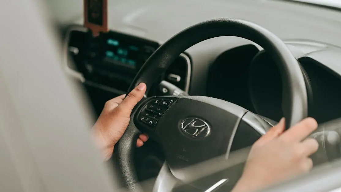 Hands Gripping A Car Steering Wheel With A Black Driving Wheel Cover Installed.