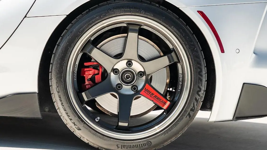 After market car part alloy wheel and red brake caliper on sports car tire in sunlight